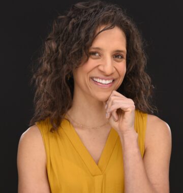 A woman with shoulder-length hair is seen in a chest-and-shoulders portrait. She wears a sleeveless golden outfit.